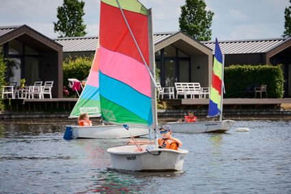 Drie kinderen die ieder in een zeilboot zitten met vel gekleurde zeilen op het Nannewiid.
