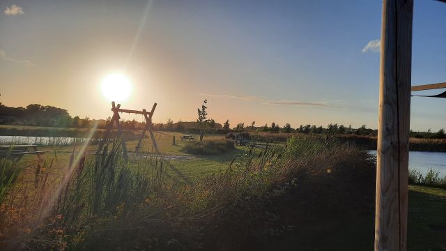 Groene speelweide met een schommel aan het water met een lage zon in de lucht bij Recreatiepark De Bosrand in Oudemirdum.