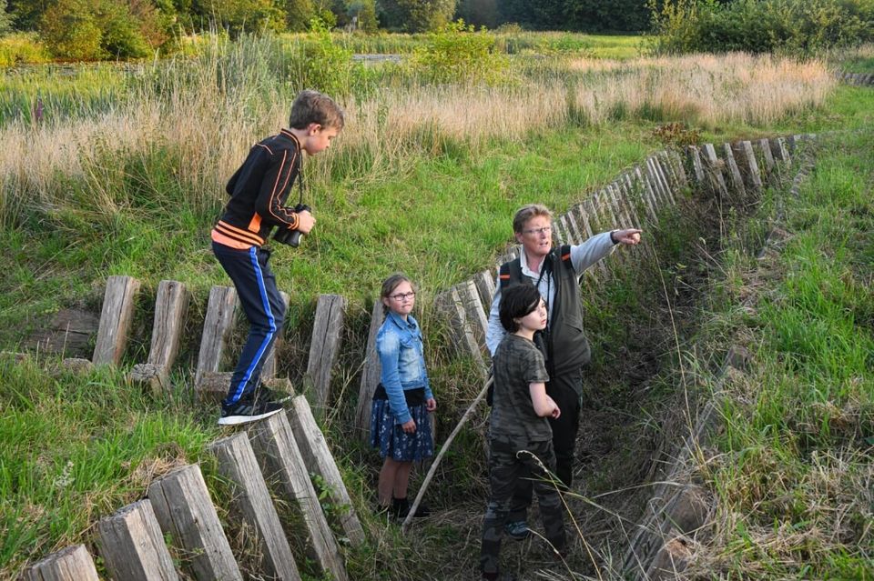 Een boswachter leidt een groep kinderen rond door een loopgraaf op een fort.