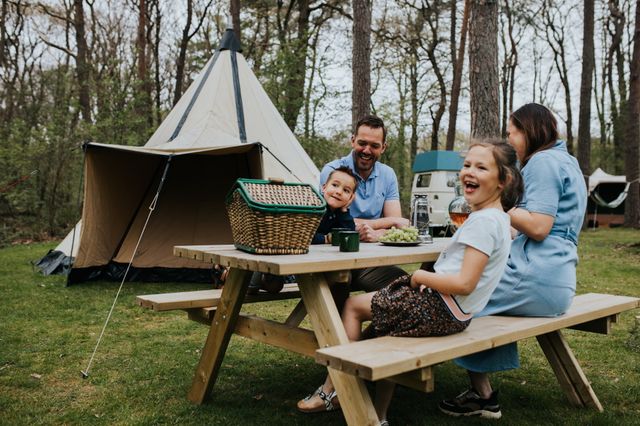 Eine Familie sitzt an einem Picknicktisch vor einem Zelt auf dem Campingplatz.