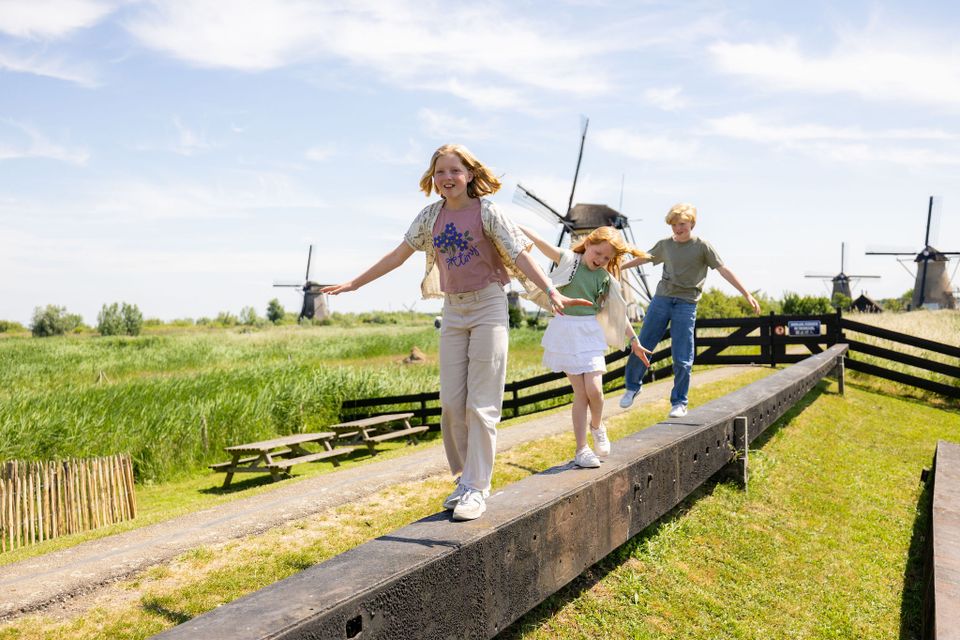 Werelderfgoed Kinderdijk, Alblasserdam, Zuid-Holland, UNESCO Werelderfgoed met historische windmolens waar kinderen balanceren op een houten balk tijdens een gezinsuitje in het Groene Hart.