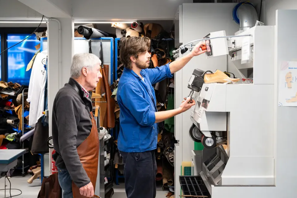Twee schoenmakers staan bij een machine met mallen en leer