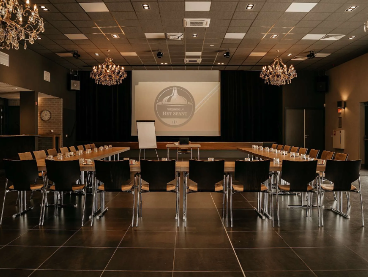 De zaal van Het Spant Ameide, er staan rijen met stoelen en een groot beamerscherm.