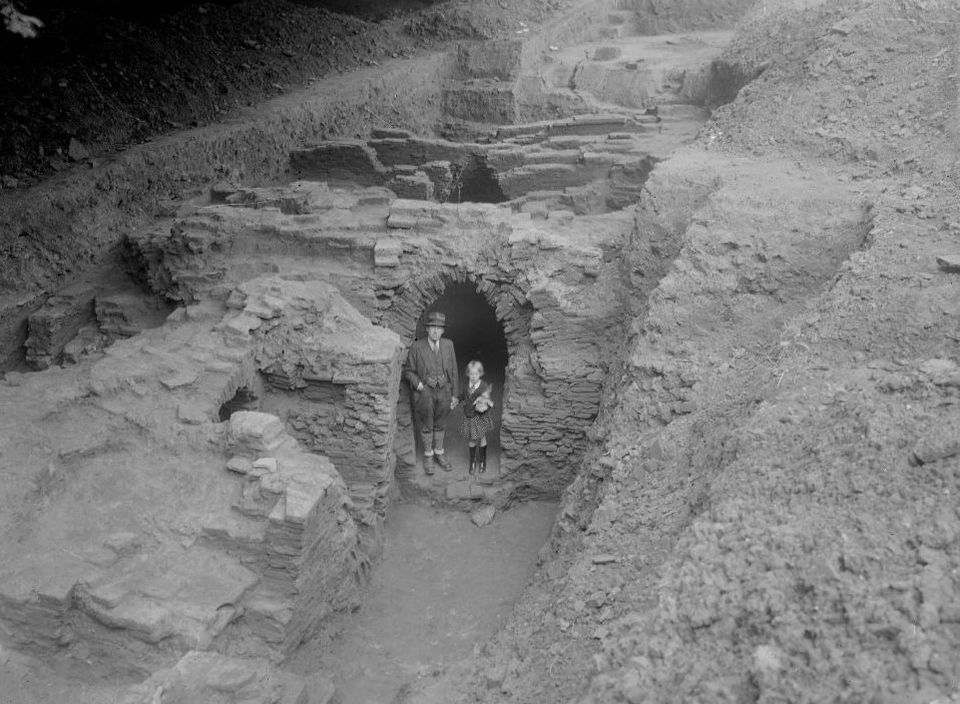Een man en een kind staan in een opgegraven pannenoven, 1942. Zwart-wit foto.