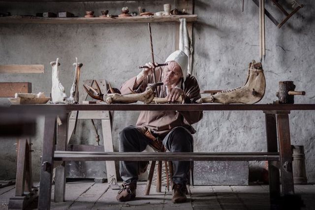 Man in middeleeuwse kleding bewerkt een hoorn met de hand in een werkplaats in Archeon, waar ambachten en historische technieken tot leven komen.