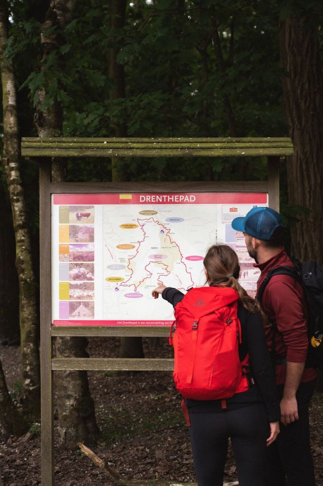 Een man en een vrouw kijken naar een bord waarop de route van het Drenthepad staat uitgestippeld