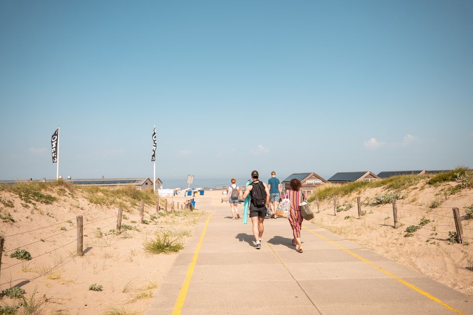 Sfeerbeeld van strandgangers die richting het strand van Katwijk wandelen met op de achtergrond een strandpaviljoen.
