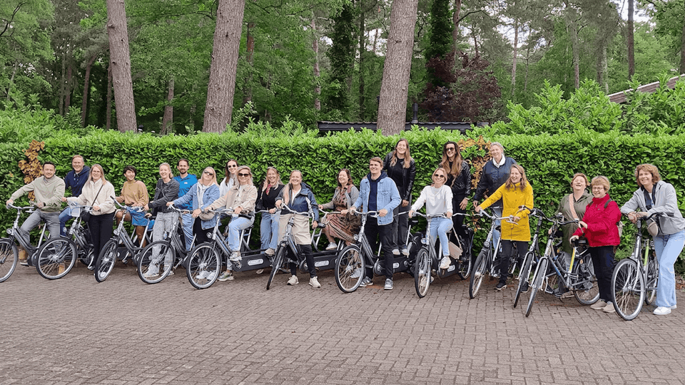 Groep fietsers staan op een rijtjes voor groene haag, klaar voor vertrek