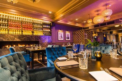 Sfeervol interieur van restaurant De Heeren van Montfoort met luxe tafels, fluwelen stoelen, warme verlichting en een uitgebreide wijnwand op de achtergrond.