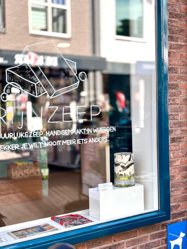 Etalage van Rijnzeep in Woerden met handgemaakte natuurlijke zeep, promotiemateriaal en raambelettering met de tekst ‘Heerlijke zeep, handgemaakt in Woerden’.