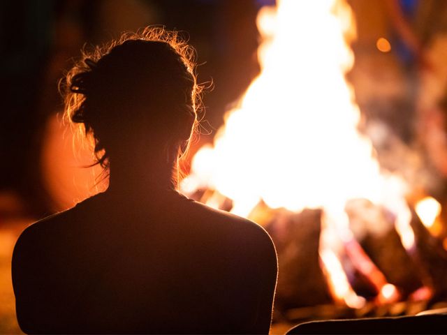 Het silhouet van een vrouw tegen een donkere hemel met een kampvuur