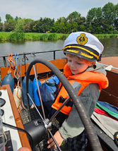 Kind met kapiteinspet aan het stuur in een boot op het water