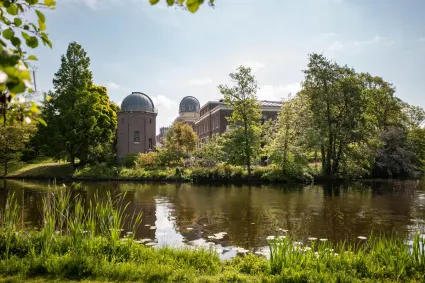 Aan de overkant van het water is tussen de bomen het oude observatoriumgebouw met koepeltorens te zien.