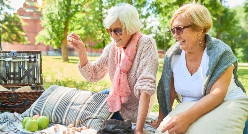 Twee oudere vrouwen zitten lachend in de zon op een picknick kleed