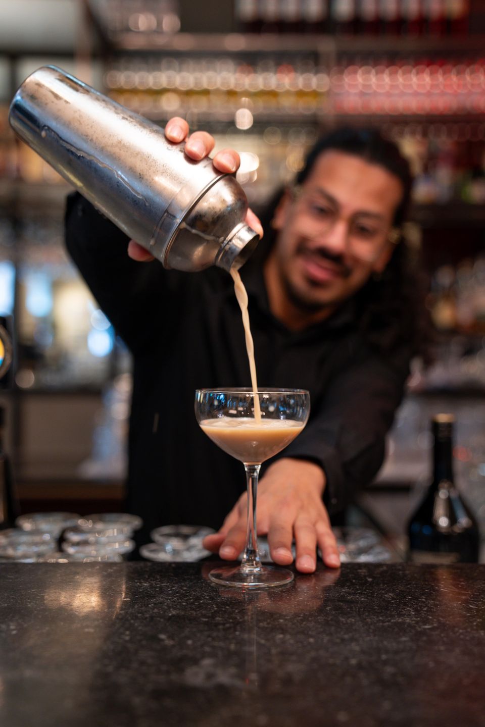 Een bar medewerker in Dudok Arnhem schenkt een verfrissende cocktail in een glas.