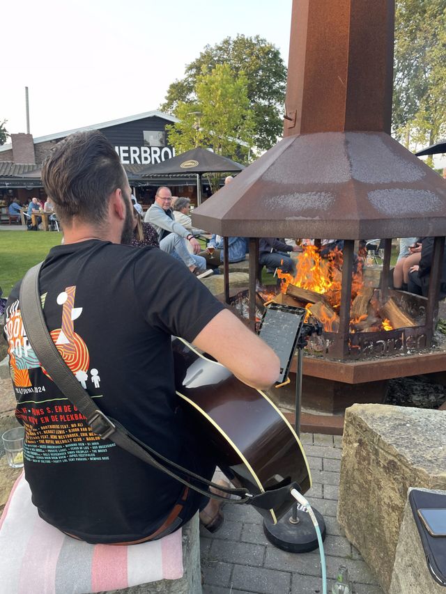 Man van achterkant met gitaar bij kampvuur