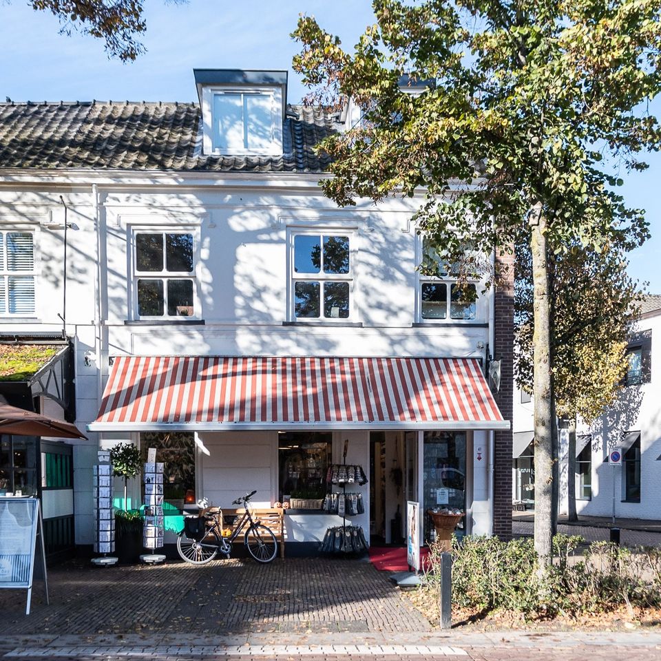 Witte gevel met afdak en boom aan de rechterkant.
