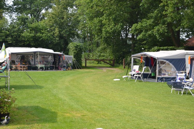 Groot groen grasveld met aan de zijkanten 2 caravans met voortenten en zitjes.