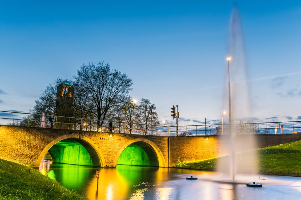 In the foreground is a water feature spanned by a bridge; behind it stands the polder tower amongst the trees in Emmeloord.