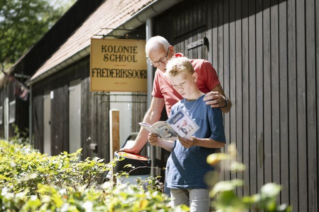 Een kind en een opa kijken naar het opdrachtenboekje van de Kolonie Fietsavontuur route