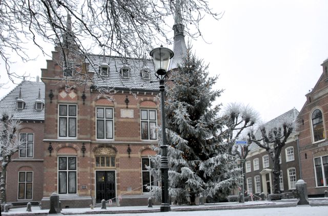 Noordwijk binnen in de winter. Er ligt sneeuw rond het monumentale gemeentehuis. In de grote denneboom, speciaal neergezet voor de kerst, branden lichtjes.