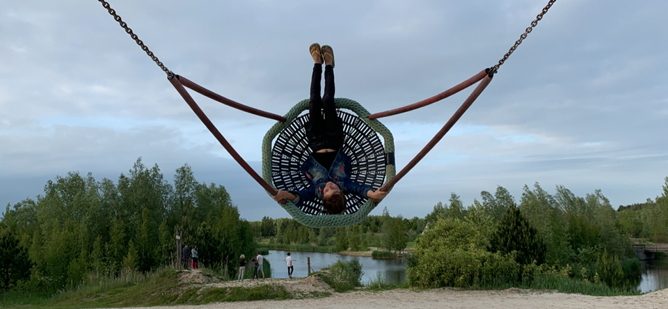 Op de voorgrond een kind op de schommel, daarachter een groene omgeving met veel water en zand in Kraggenburg in de Noordoostpolder.