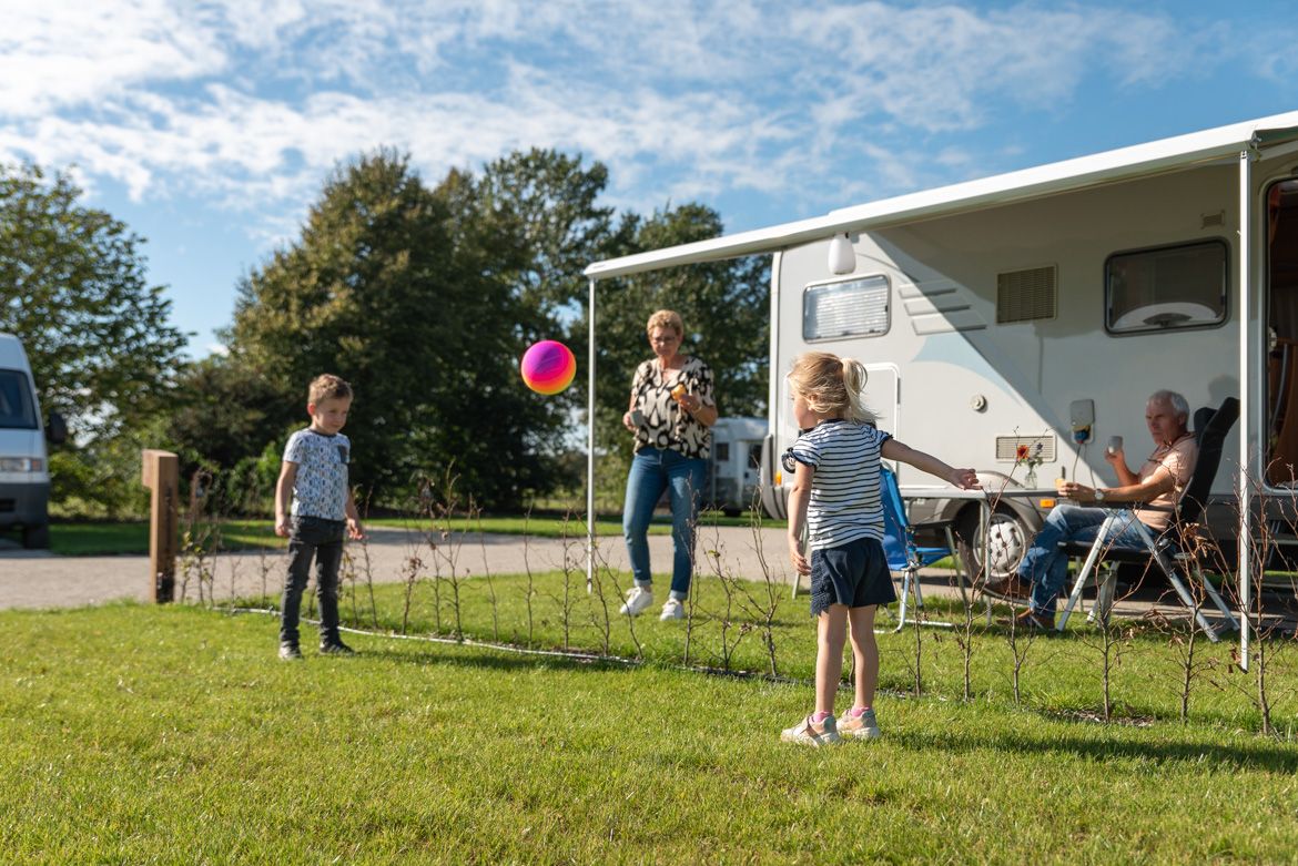 Caravan op een grasveld met spelende kinderen op de voorgrond.