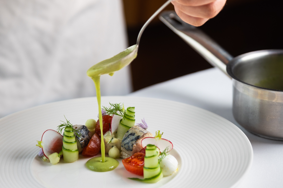 De kok maakt een culinair gerecht af met een lepel.