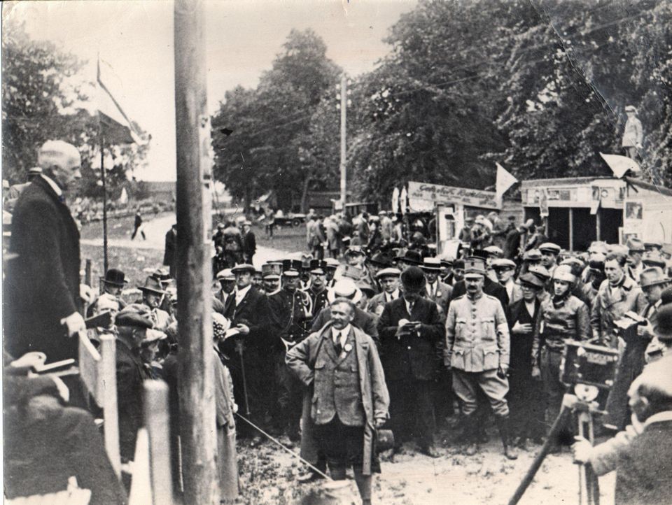 Links de Commissaris van de Koningin in Drenthe, dhr. J.T. Linthorst Homan, tijdens de opening van de eerste TT-races te Rolde. Op de achtergrond een groot aantal personen. De man met de hoed in de hand is G. Kramer, bestuurslid van de TT organisatie.