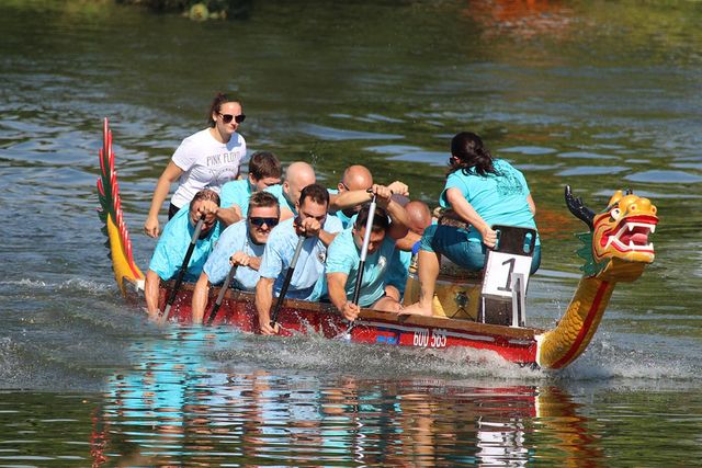 Een team peddelt vol kracht in een kleurrijke drakenboot tijdens een zomerse waterwedstrijd in Woerden