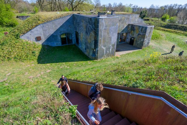 Bezoekers beklimmen een trap naast Fort Kijkuit in Kortenhoef. Het fort is slechts deels zichtbaar, doordat het schuil gaat in de heuvelachtige omgeving.