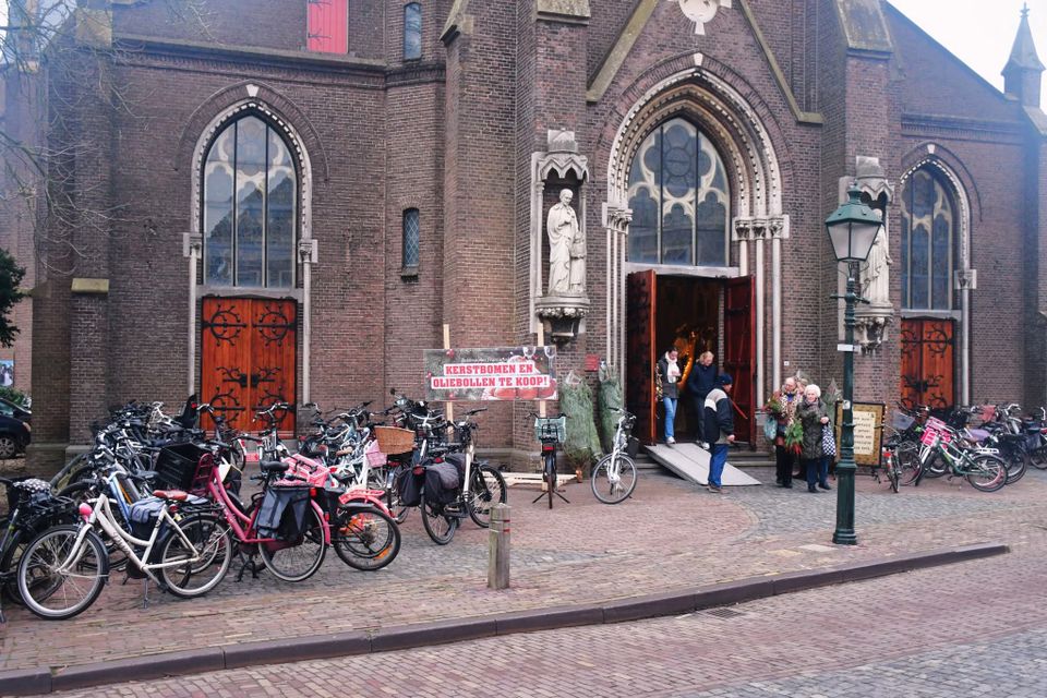 Kerstmarkt bij de Sint-Franciscuskerk in Oudewater, Groene Hart, met bezoekers bij de ingang van de historische bakstenen kerk, kerstbomenverkoop en geparkeerde fietsen.