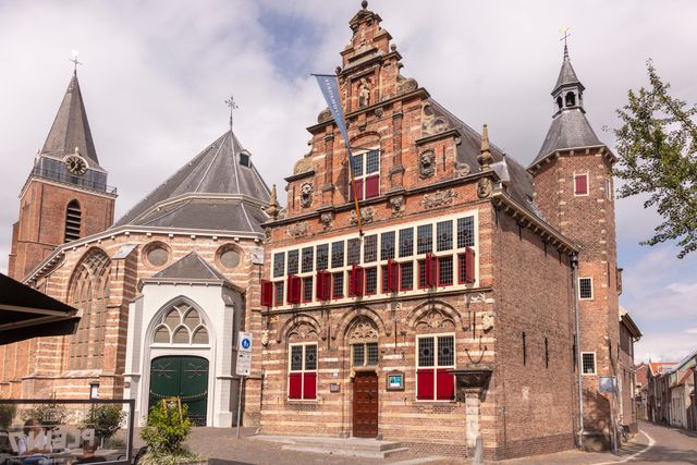 Voorgevel van het Stadsmuseum Woerden met historische raampartijen en rode luiken, naast de Petruskerk op een zonnige dag