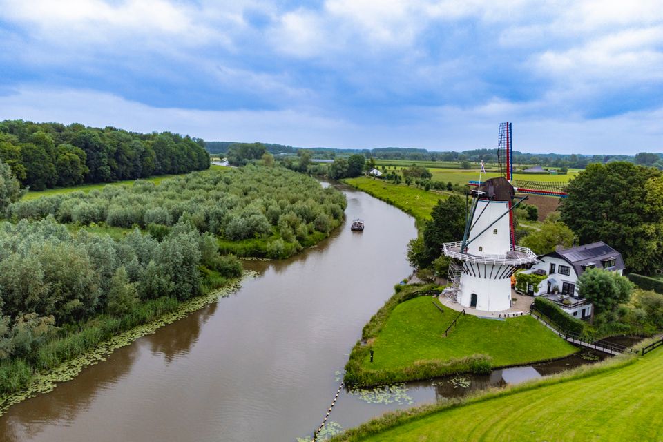 Over de brede rivier de Linge vaart een boot, rechts is een molen te zien.