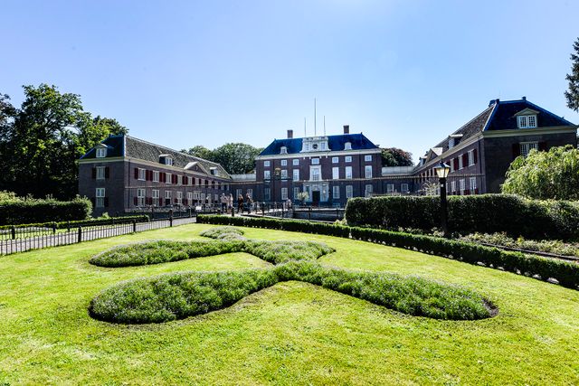 De voorkant van Slot Zeist met een blauwe poort en groen park