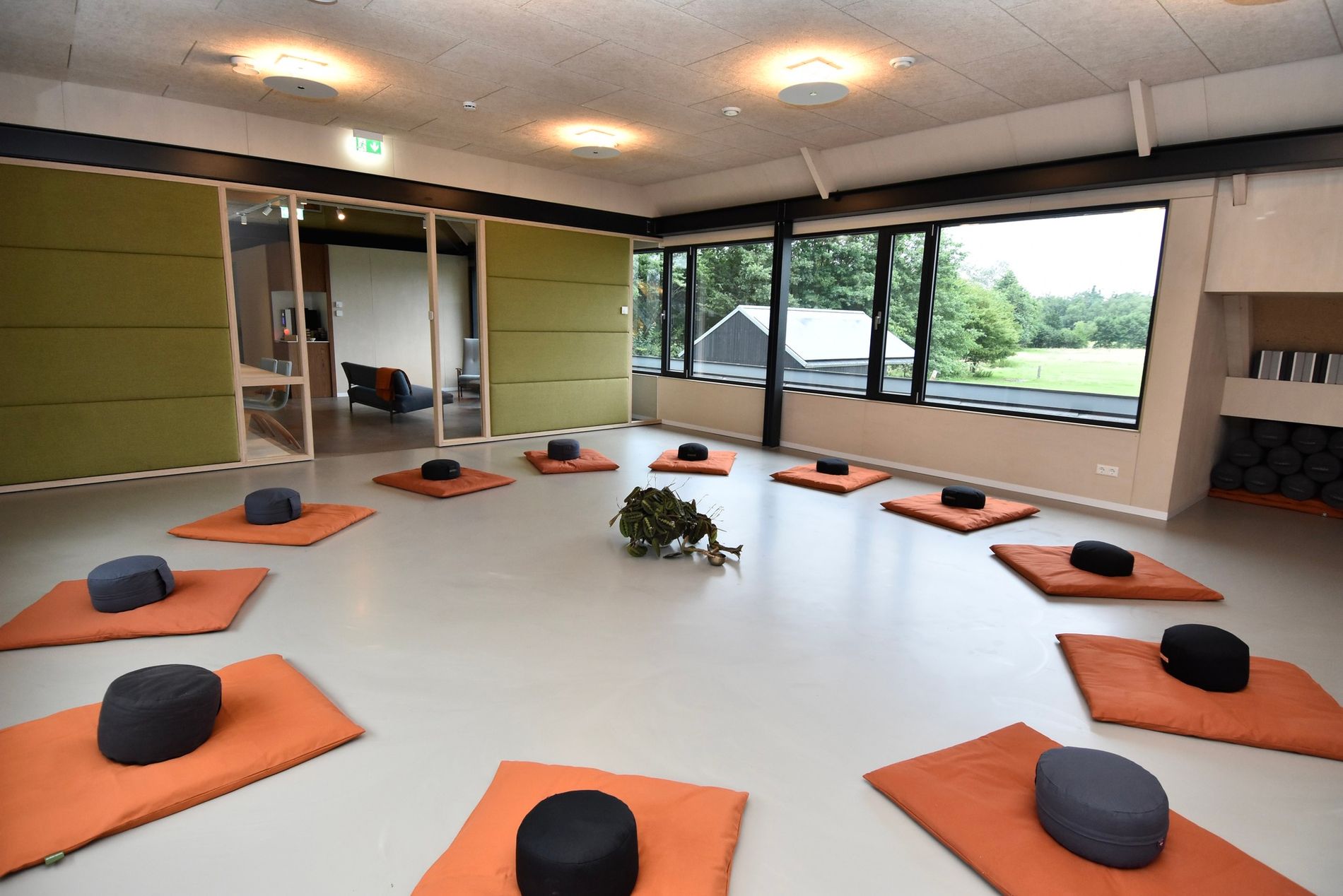 Een lichte ruimte met op een witte vloer oranje matjes en zwarte kussentjes.