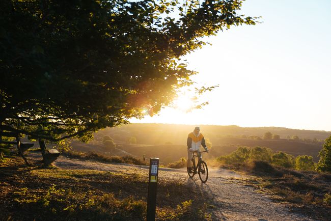 Man fietst door een prachtig, open natuurgebied waar de zon langzaam ondergaat