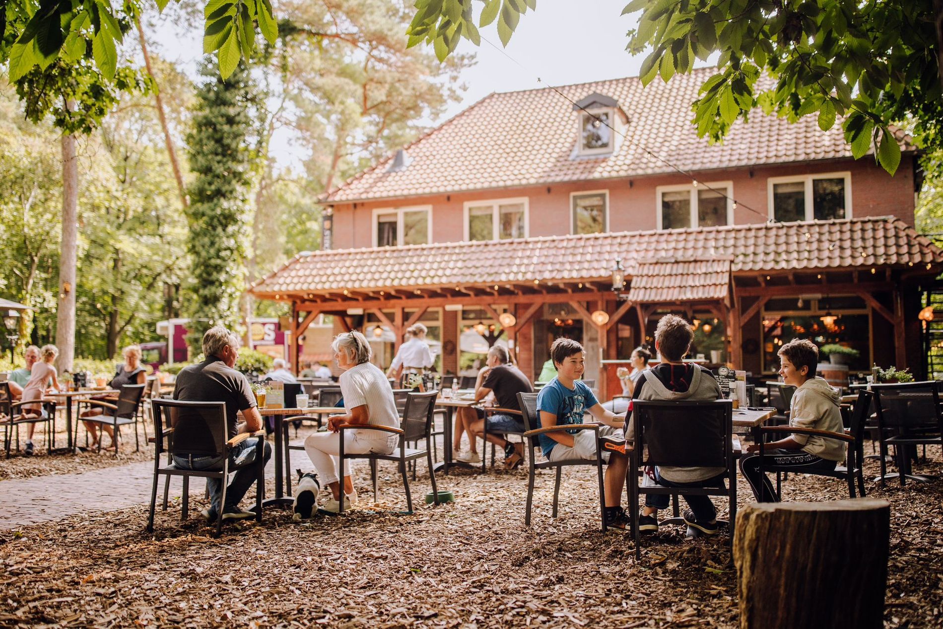 Terras in bosrijke omgeving met het hotel-restaurant op de achtergrond.