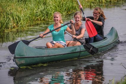 Drie vriendinnen kanoën lachend door een smal watertje tussen het riet bij Boerderij de Boerinn in het Groene Hart.