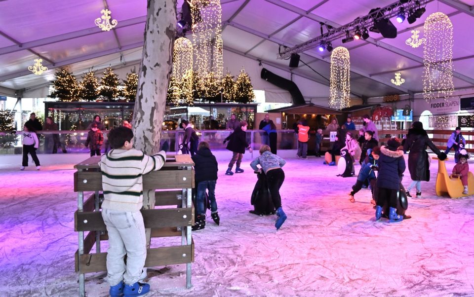Kinderen en volwassenen schaatsen op de sfeervol verlichte Rotary-ijsbaan op het Kerkplein in Woerden.