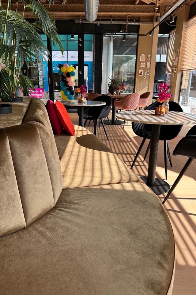 Een lange bank met tafeltjes en stoelen waaraan mensen kunnen eten in een lunchcafe in Emmen.