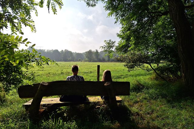 Boswachter Ellen haar vriendin en dochter op een bankje kijkend naar een uitgestrekt mooi groen grasveld