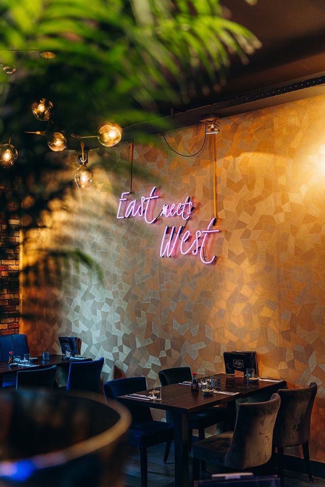 Sfeervol interieur van Restaurant Mido in Woerden met neonlamp "East meets West" aan de muur en gedekte tafels.