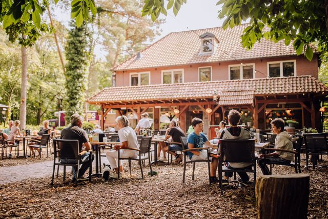 Terras in bosrijke omgeving met het hotel-restaurant op de achtergrond.
