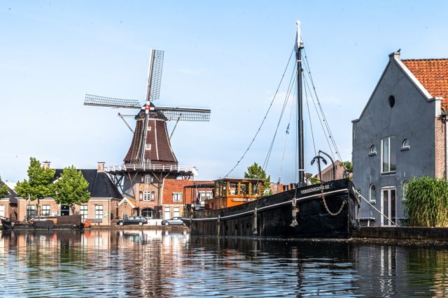 Gracht in een dorp met boot in het water en molen op de achtergrond.