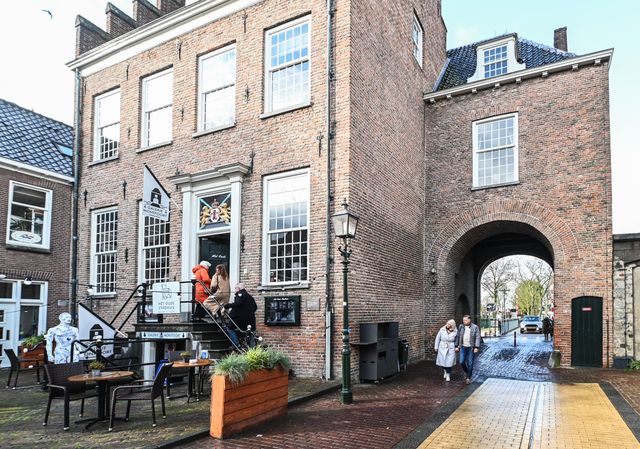 Historisch Oude Stadhuis in Montfoort aan de binnenstad, met mensen die de trap opgaan en wandelaars onder de stadspoort. Voor het gebouw staan terrastafels. Het is een sfeervolle plek in de middeleeuwse vestingstad Montfoort.
