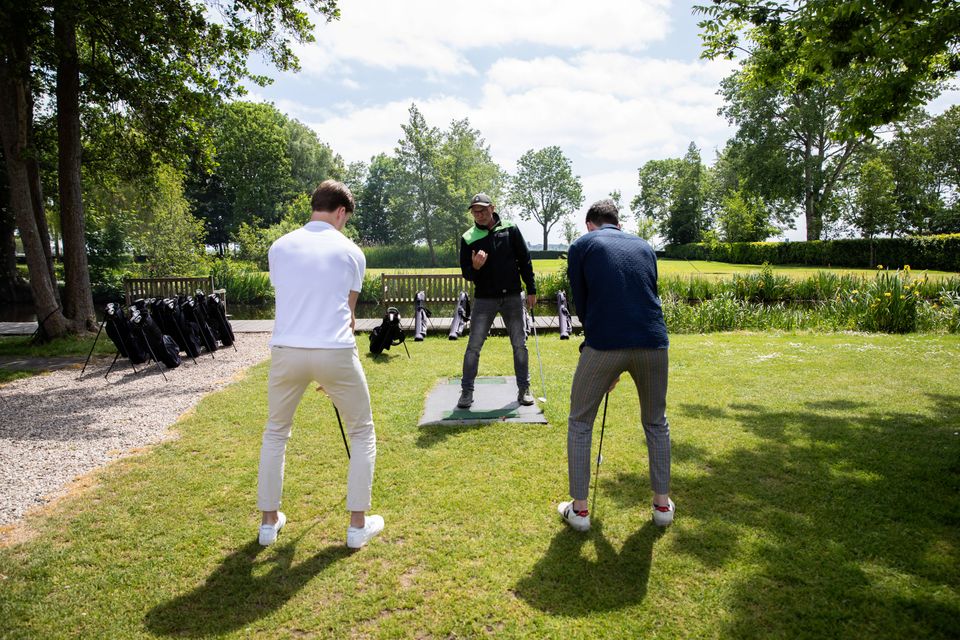 Instructeur geeft golfles aan twee deelnemers tijdens een golfclinic op het groene terrein van Buitenplaats Kameryck