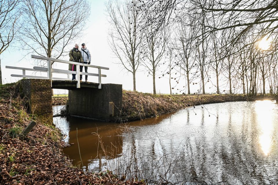 Wandelaars op een wit bruggetje bij Landgoed Linschoten, uitkijkend over een rustige waterloop omgeven door kale winterbomen en zacht zonlicht; een rustige wandelervaring in het Groene Hart.