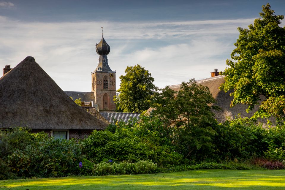Rietgedekte boerderijen met op de achtergrond een kerktoren.