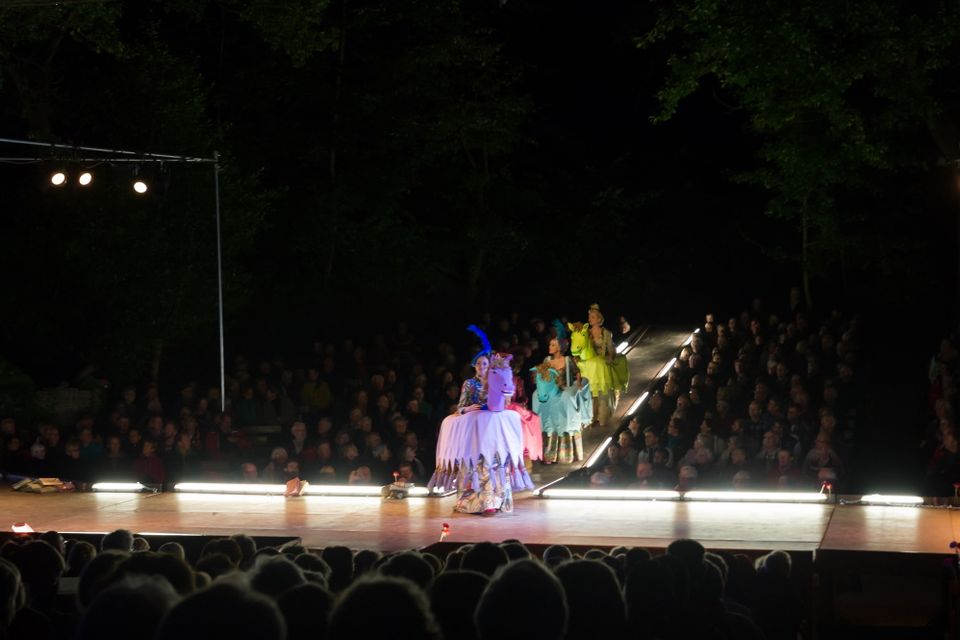 Acteurs staan op het podium van het openluchttheater en het publiek kijkt aandachtig toe.